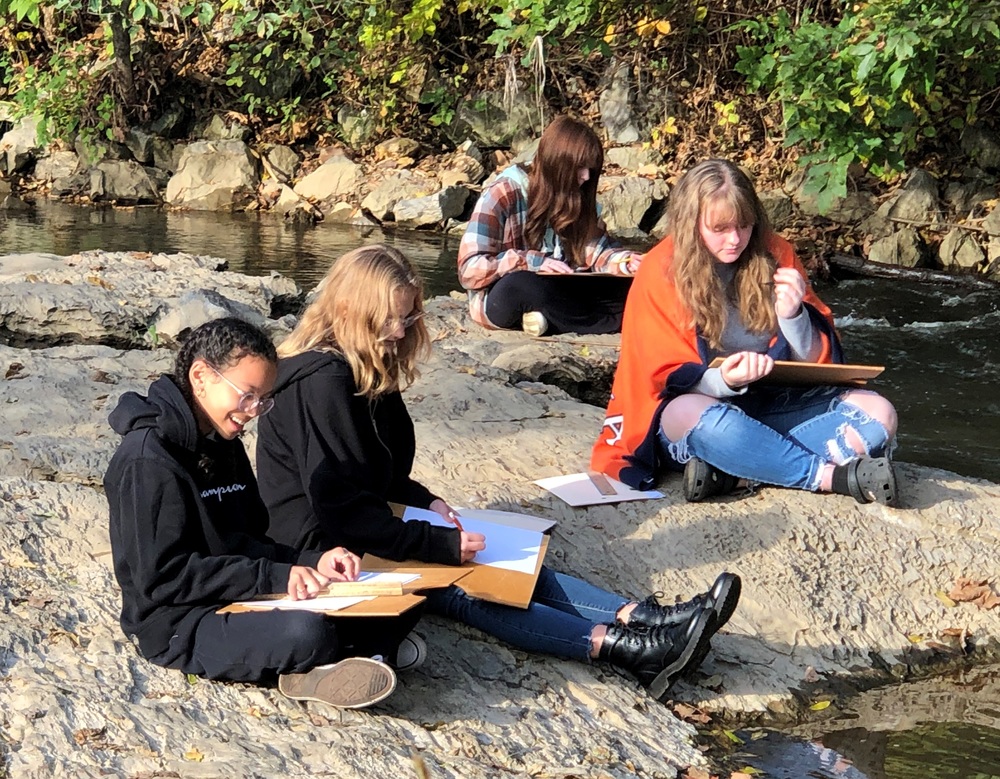 students sitting by the creek bed painting and journaling 