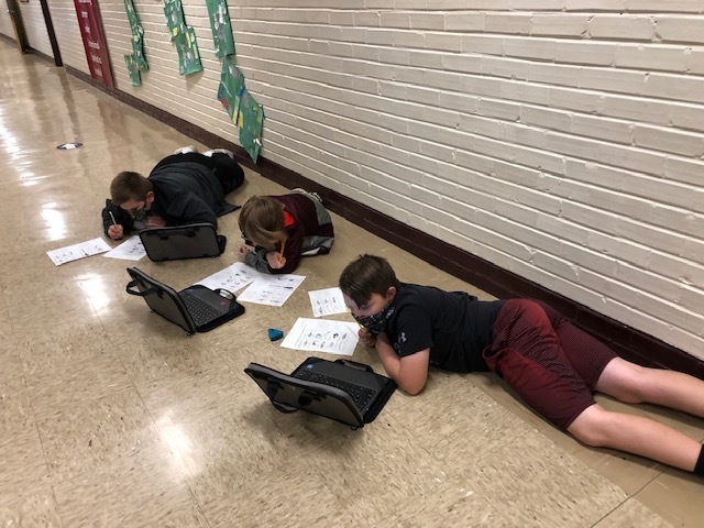 students working on chromebooks on the floor in the hallway